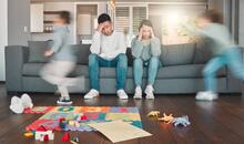 Pareja de padres exhaustos sentados en el sofá con gesto de agotamiento mientras sus hijos corren a su alrededor, ilustrando el burnout parental