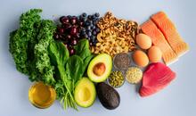 Vista cenital de alimentos antiinflamatorios como salmón, atún, kale, espinacas, aguacate, arándanos, nueces, semillas, huevos y aceite de oliva sobre fondo claro