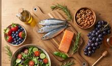 Sardinas, salmón, frutos rojos, uvas, frutos secos, ensalada y aceite de oliva sobre una mesa de madera en representación de alimentos que forman parte del patrón de la nutrición antiedad.