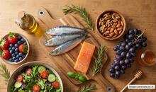 Sardinas, salmón, frutos rojos, uvas, frutos secos, ensalada y aceite de oliva sobre una mesa de madera en representación de alimentos que forman parte del patrón de la nutrición antiedad.
