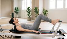 Mujer haciendo footwork en una máquina de pilates reformer en una sala específica para esta actividad, en representación de la comparativa de pilates reformer vs mat